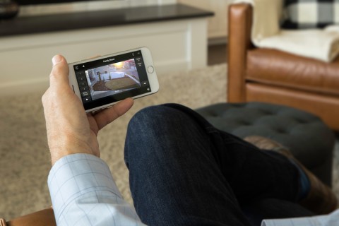Closeup of a man using his smartphone to monitor a front yard security camera. 
