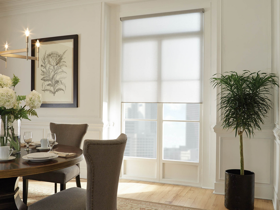 A Lutron motorized shade drawn halfway over a window in a dining room.