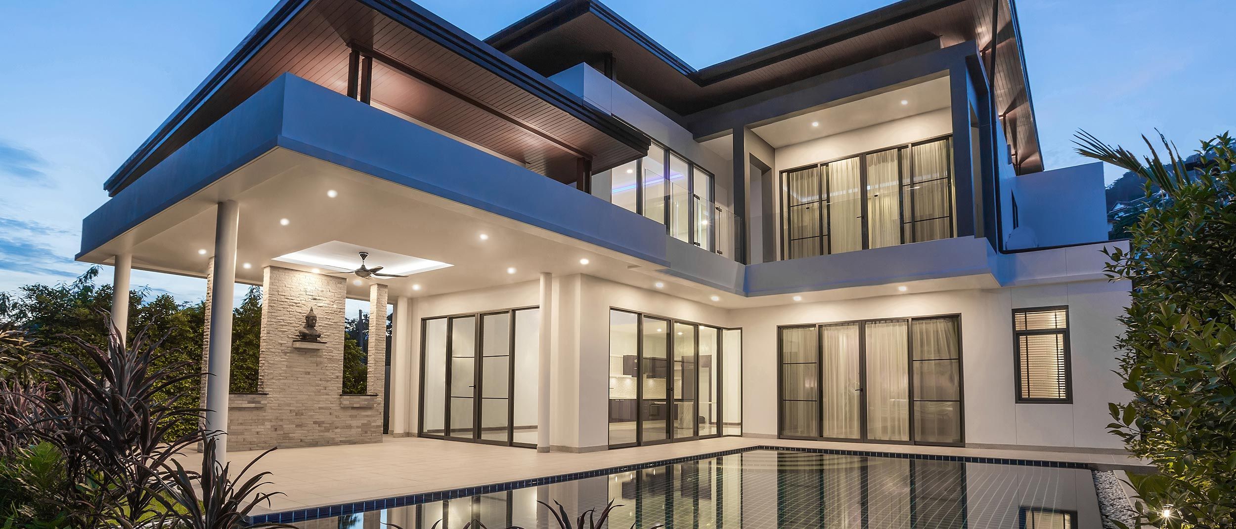 Modern two-story home with extensive glass walls and warm exterior lighting